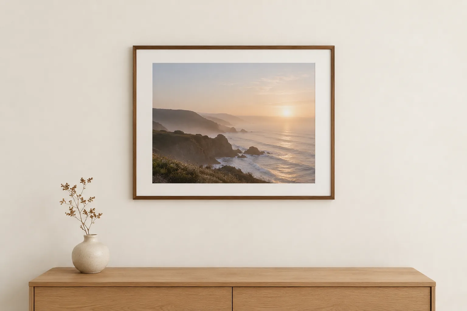 A framed landscape photograph hanging on a warm off-white wall above a wooden sideboard